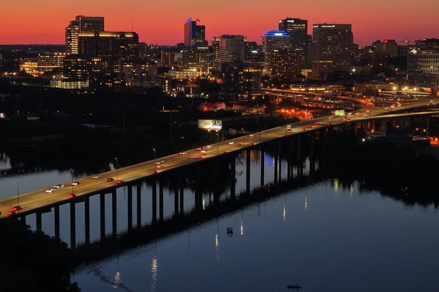 Richmond skyline at dusk with illuminated buildings, highway bridge and river reflection.